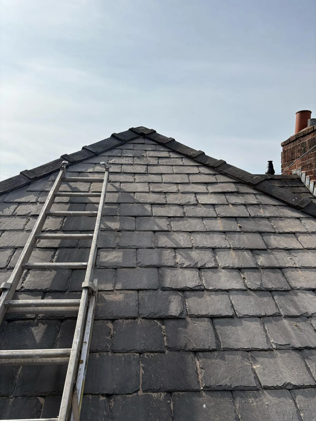 Slate roof with a roof ladder hooked over the ridge and a chimney stack behind