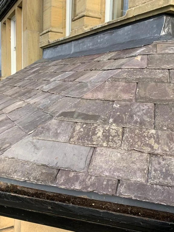Slate roof over a bay on a stone house, with lead flashing at the top and the gutter along the eaves