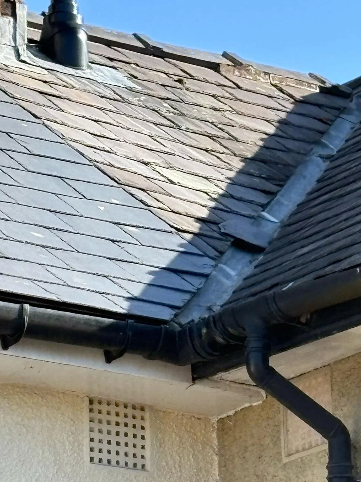 Slate roof hip coming down to the eaves, with the gutter and downpipe below a rendered wall