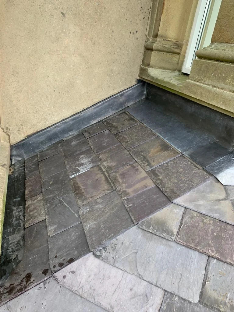 Slate roof meeting a rendered wall at a lead flashing, beside a window