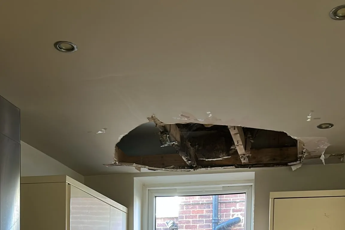 Collapsed kitchen ceiling with the plasterboard broken away, exposing the timber joists after a leak