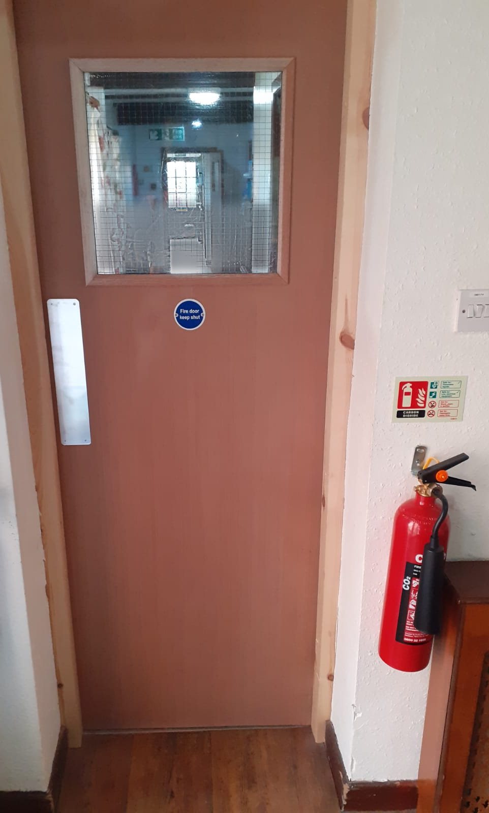 Glazed FD30 fire door with a wired-glass vision panel, push plate and fire door keep shut sign in a new timber frame, with a fire extinguisher on the wall beside it