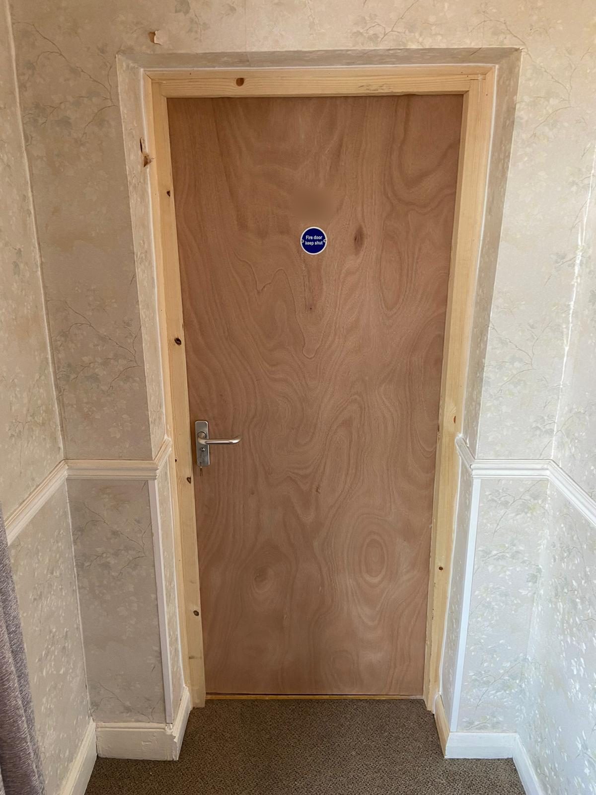 New plywood flush FD30 fire door to a care home bedroom, with a lever handle and a fire door keep shut sign, in an undecorated timber frame