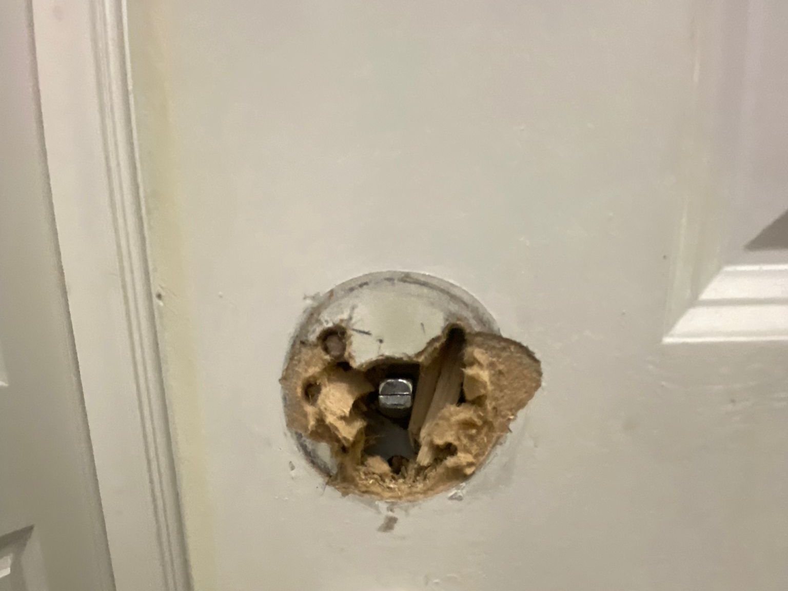 Close-up of a white panelled door where a handle has pulled out, leaving a ragged hole with torn material and old screw holes round its edge