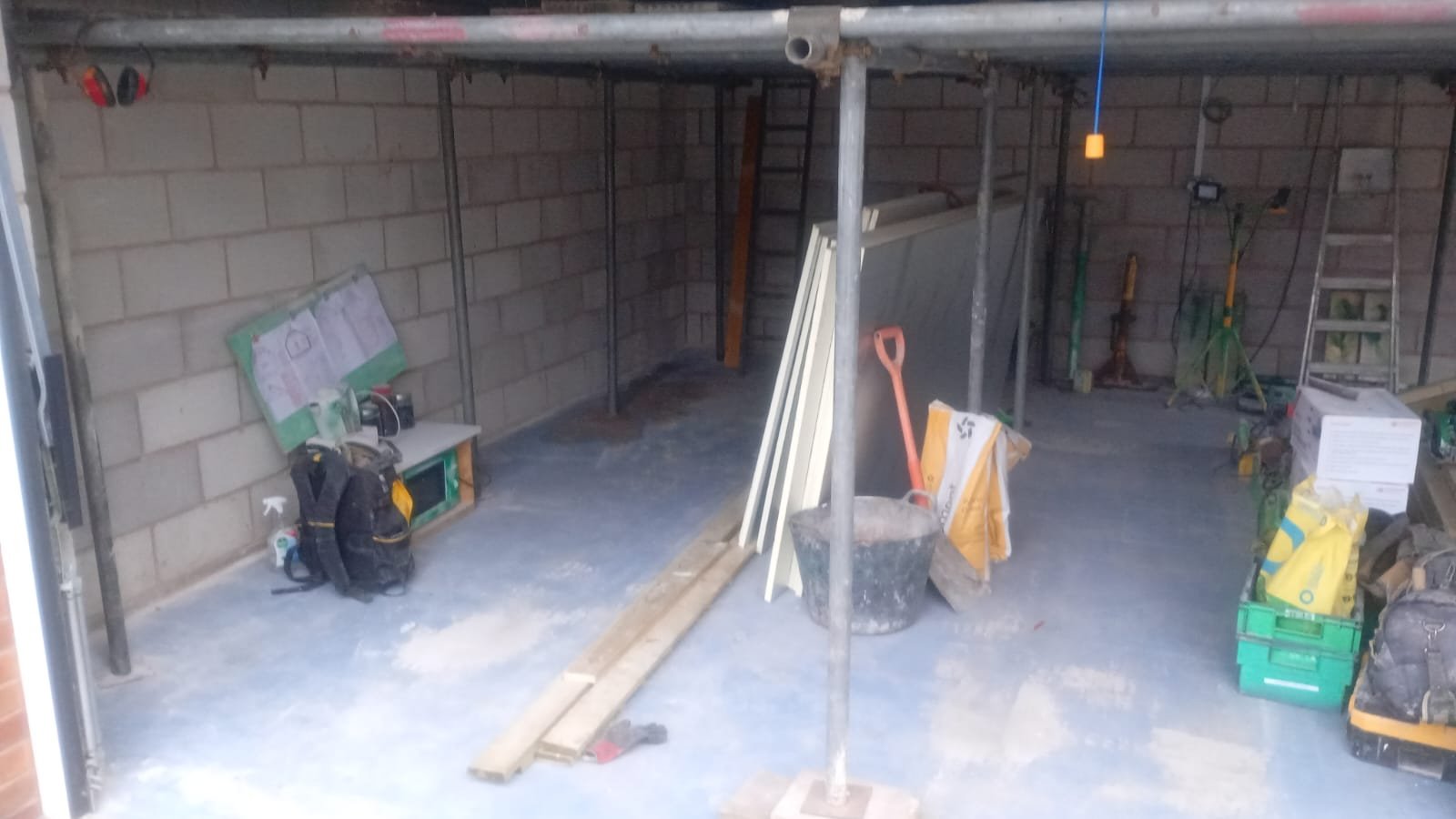 Bare blockwork garage interior with a temporary load-bearing scaffold platform installed before structural alteration work