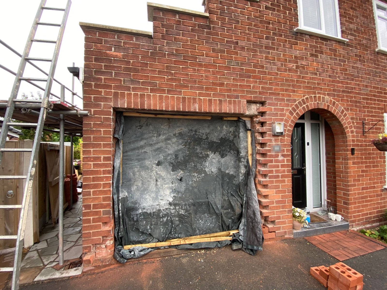 Garage door removed from a brick house with a new lintel installed above the opening and the head of the opening infilled in matching brick