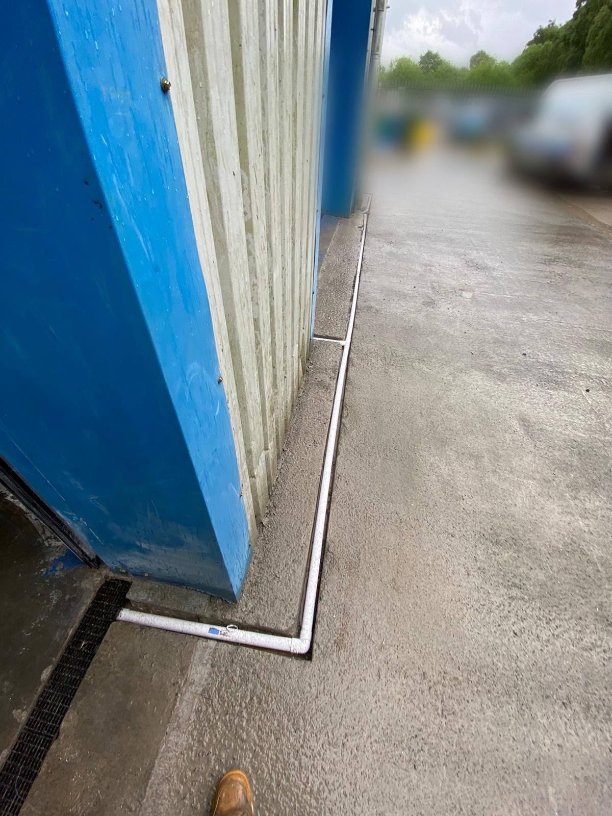 New plastic channel drain laid along the base of profiled metal cladding on a commercial unit, connected into an existing grated yard channel