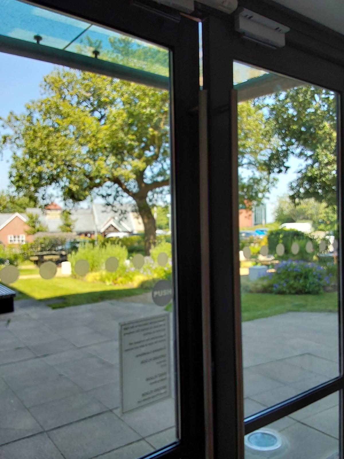Pair of glazed doors in dark metal frames seen from inside, with magnetic locks at the head and a garden and car park beyond