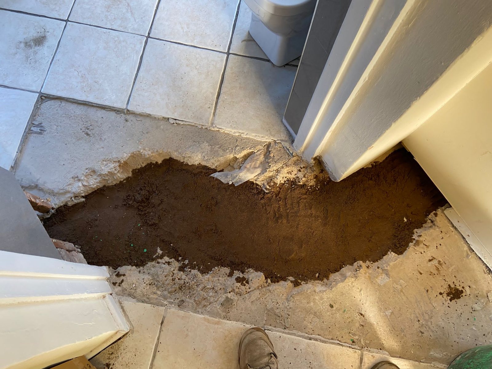 Tiled concrete floor broken out in a doorway, showing dark damp fill beneath