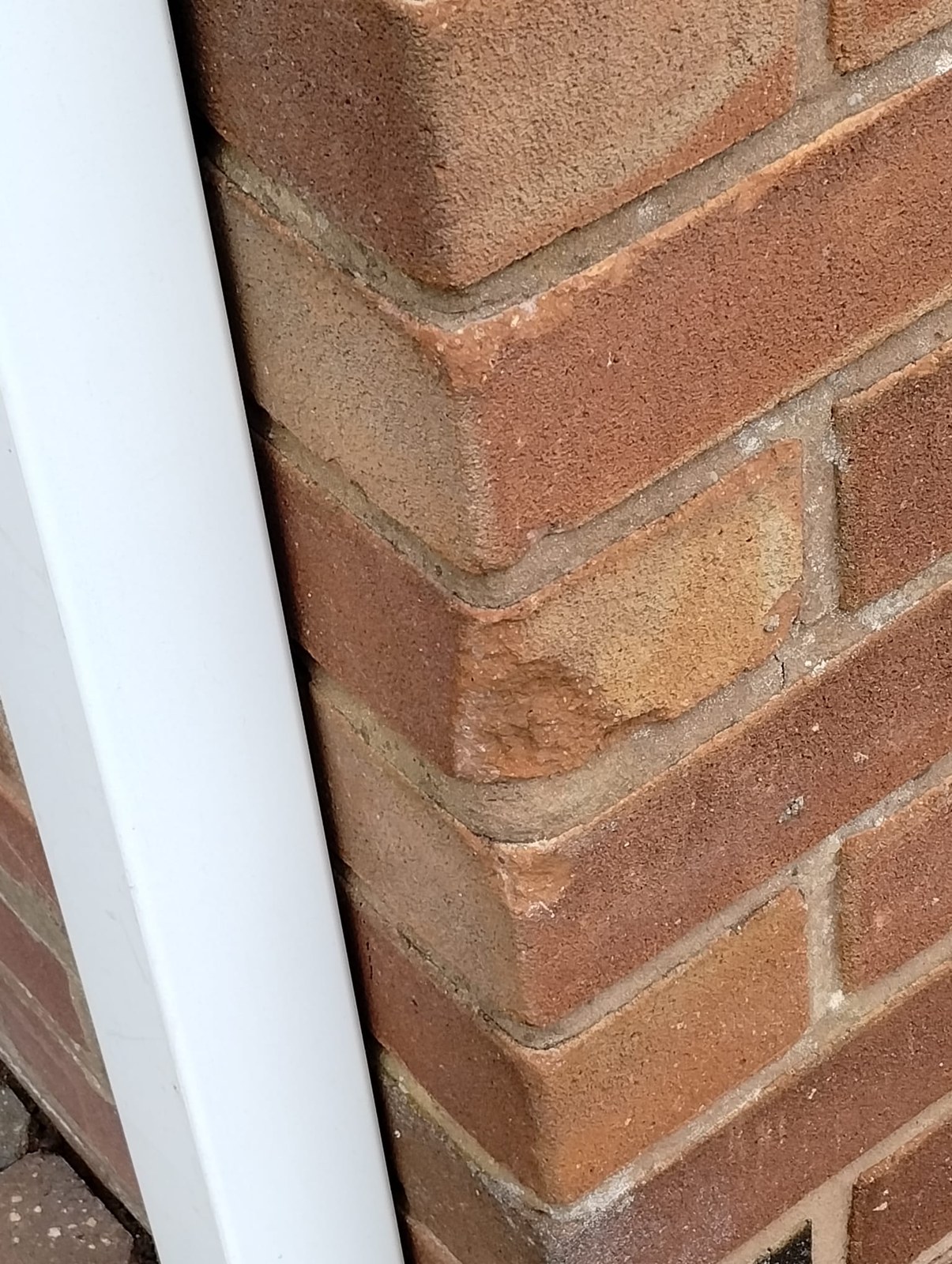 Brick repair in Flintshire – chipped bricks beside the downpipe before Close view of a red brick corner beside a white downpipe, showing chipped brick edges and a cracked joint