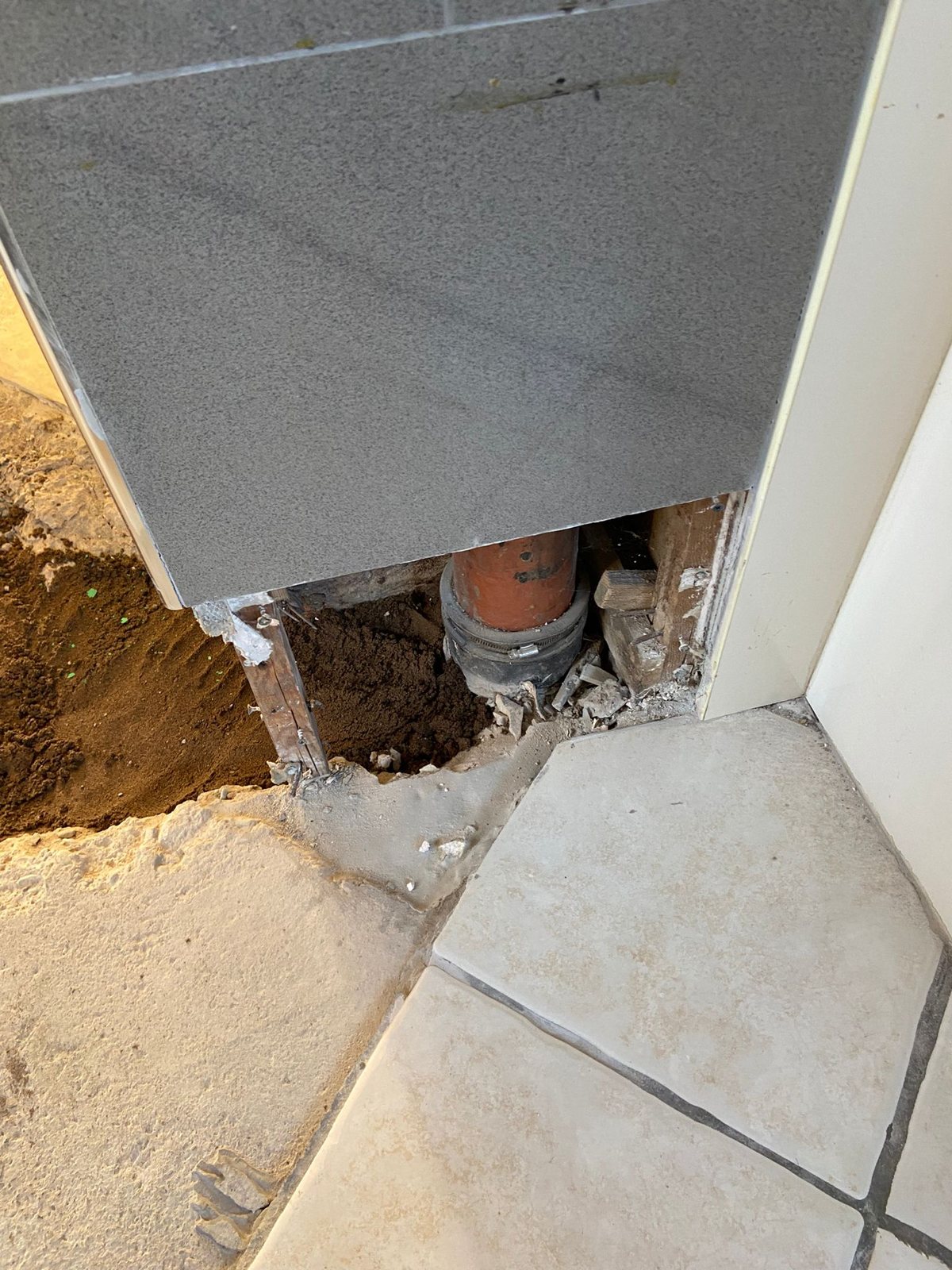 Clay drain pipe with a rubber coupling exposed below a tiled boxing where a concrete floor has been broken out