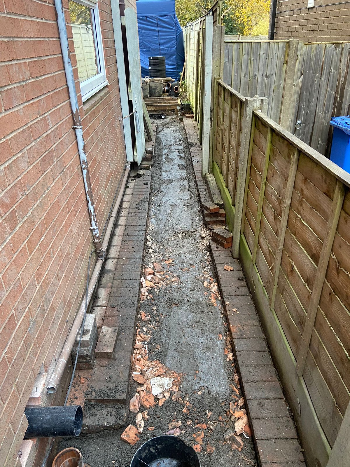 Trench excavated along a narrow side path beside a house to install a new drainage run during a garage conversion