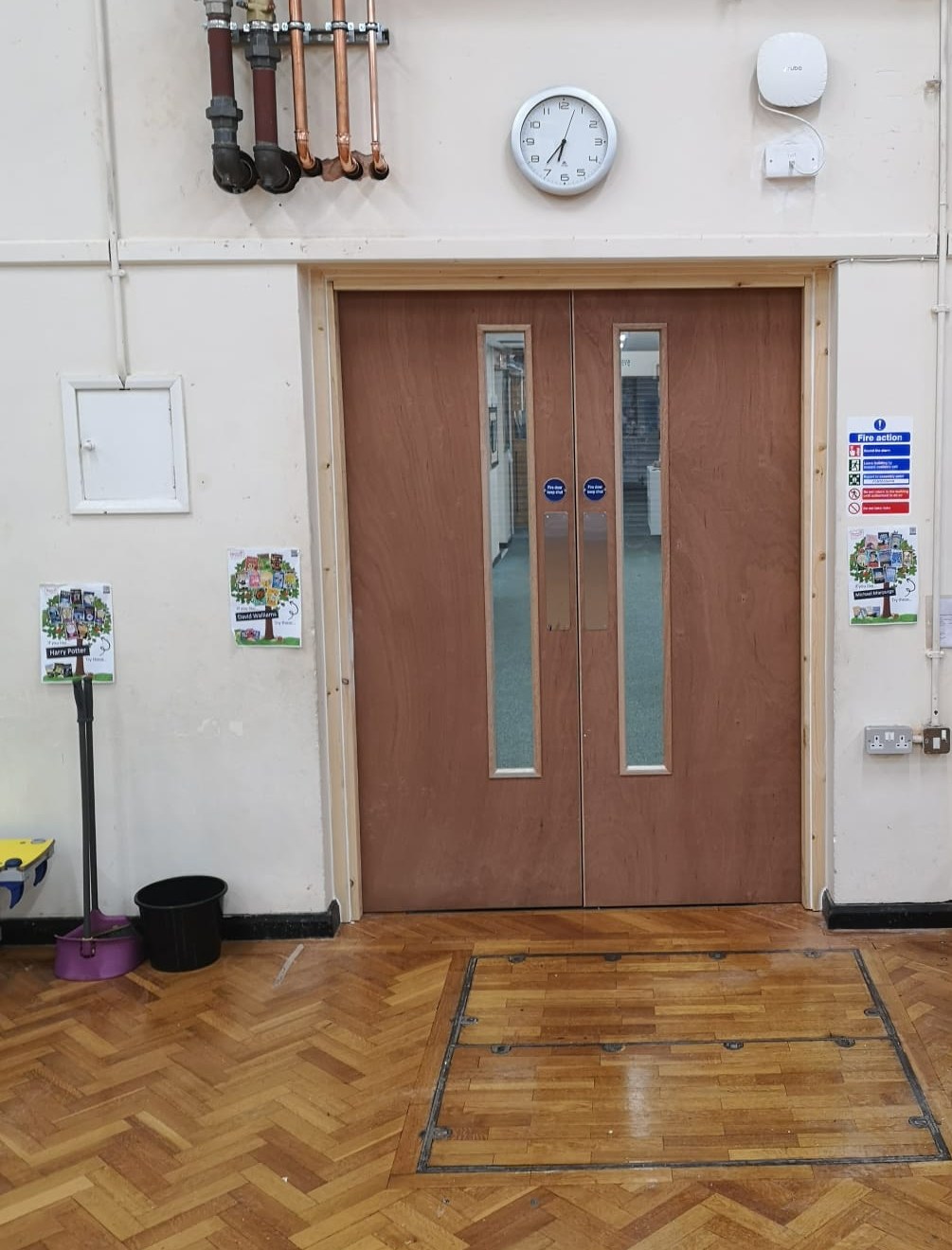 Pair of plywood-faced FD30S fire doors with narrow vision panels in a new timber lining, in a school hall wall