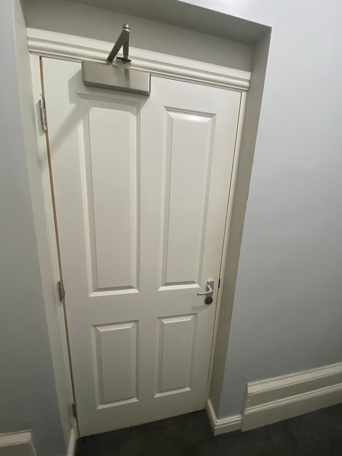 White four-panel front door with an overhead door closer and a lever handle on a backplate