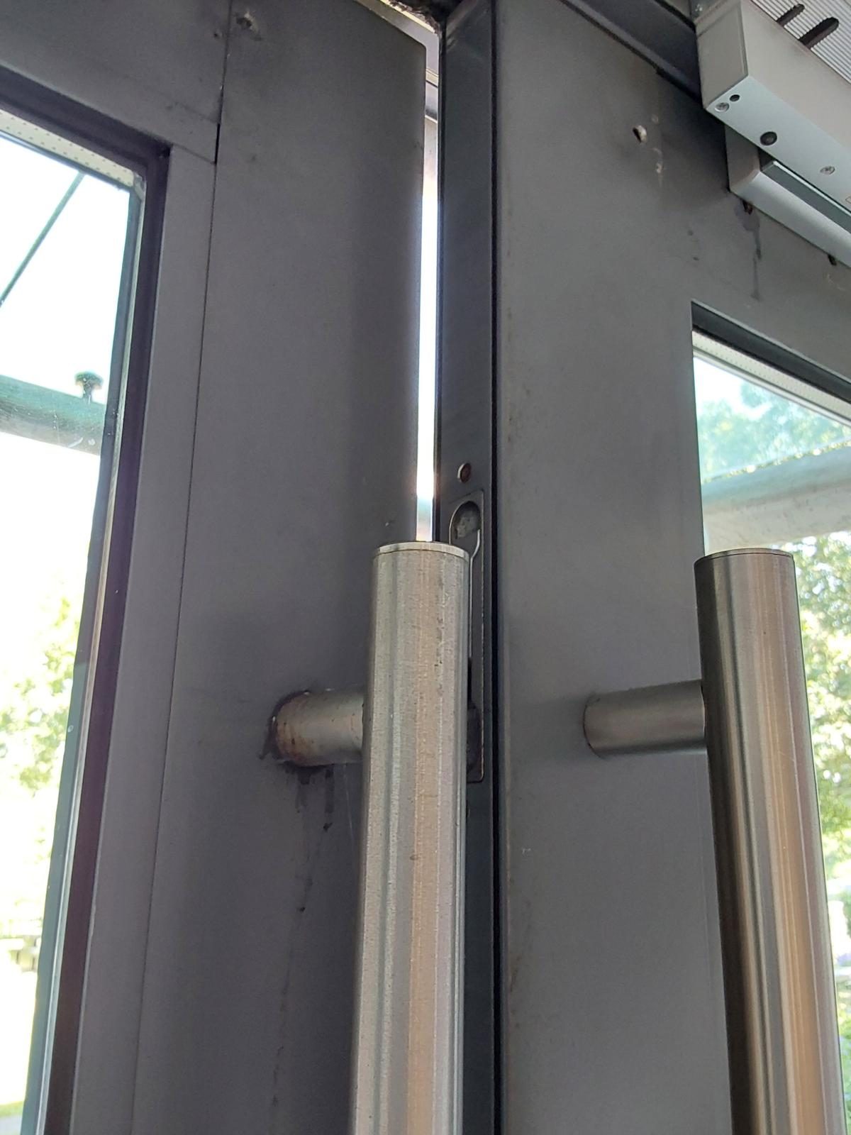 Close-up of the meeting stiles of a pair of glazed doors, with pull handles, a magnetic lock at the head and daylight showing between the leaves at the top