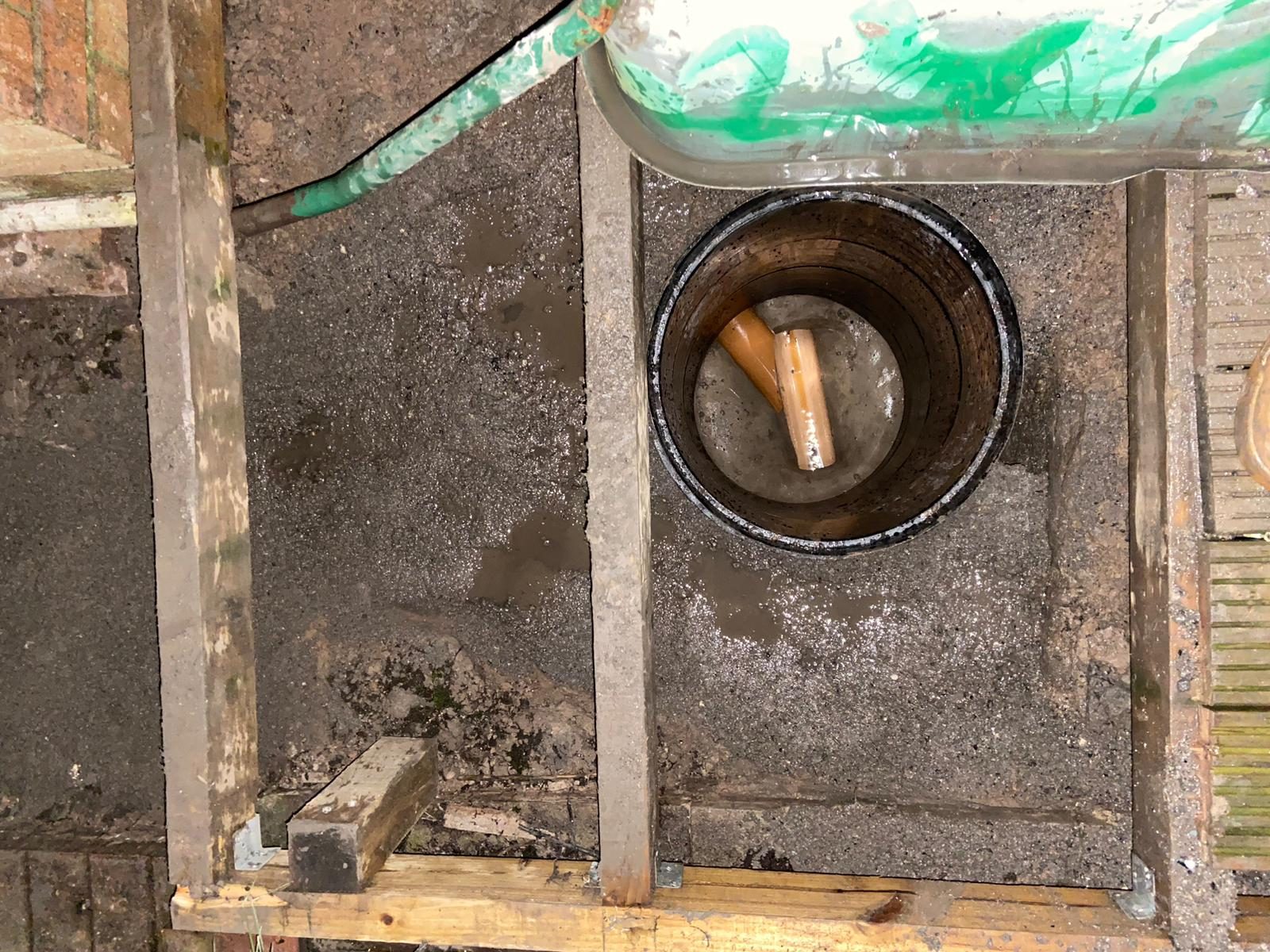 Looking down into a new drainage chamber set in concrete inside a timber frame, with orange pipe visible at the bottom of the shaft