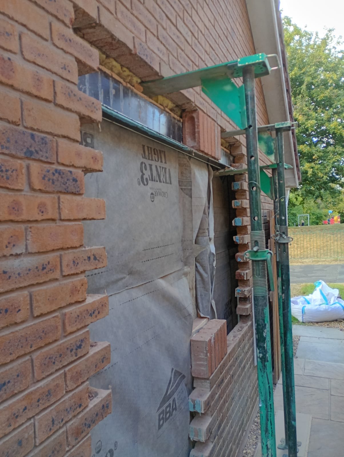 New opening being formed in the brickwork of a detached garage, propped on adjustable supports with a lintel installed and breathable membrane behind