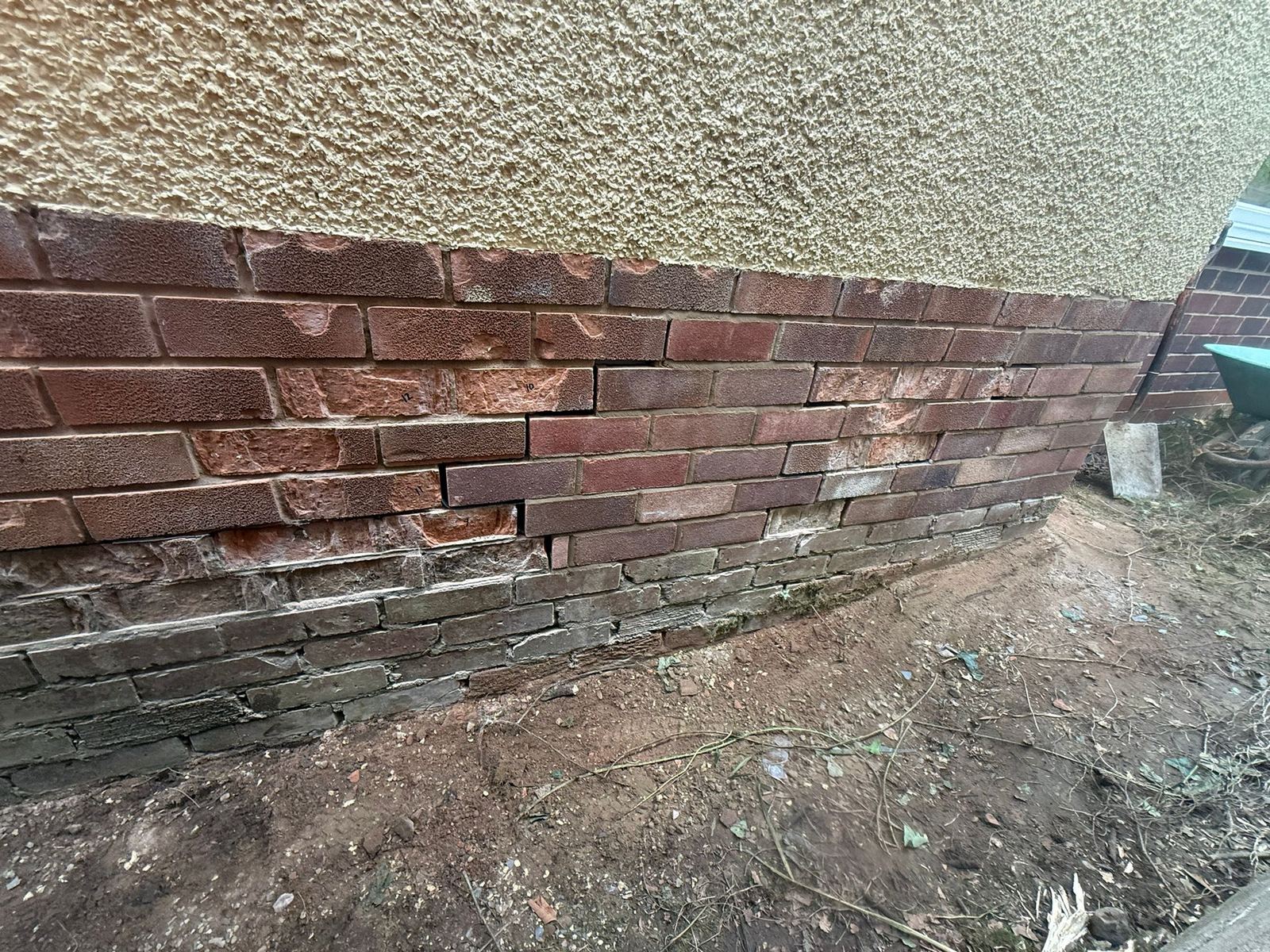 Brick plinth part-way through repair, with new bricks laid on the right and spalled bricks on the left marked with handwritten numbers