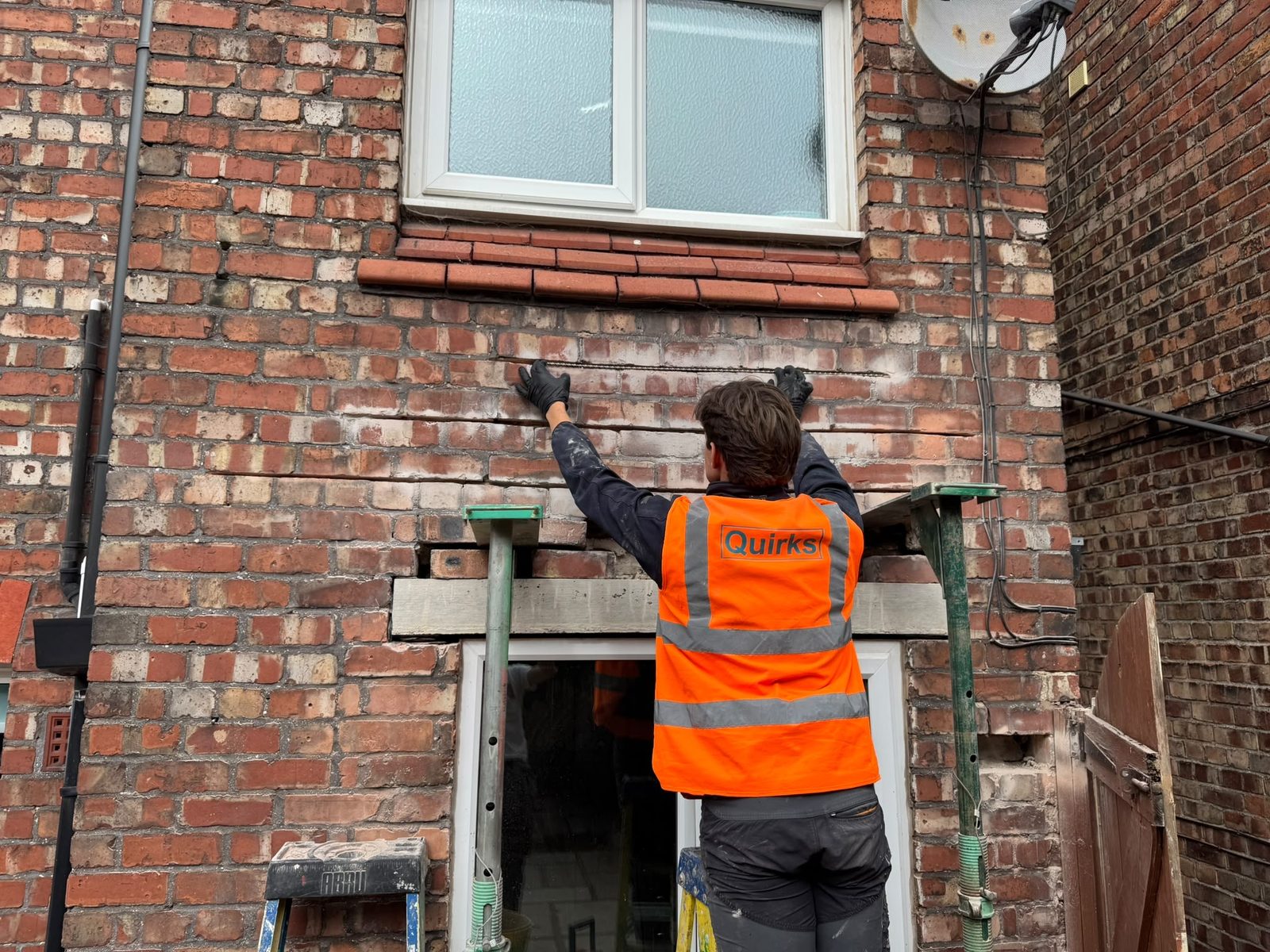 Quirks operative fitting a reinforcement bar into a brickwork joint above a propped door opening