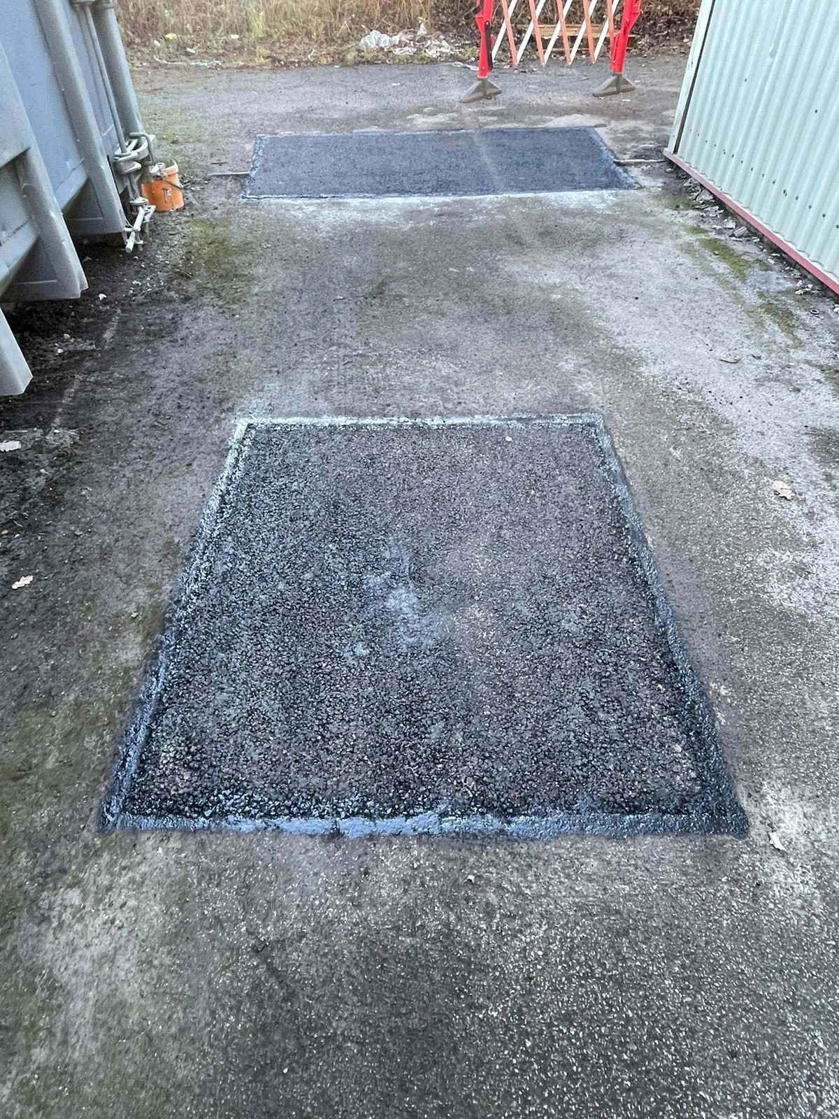 Two fresh tarmac patch repairs on an industrial yard surface