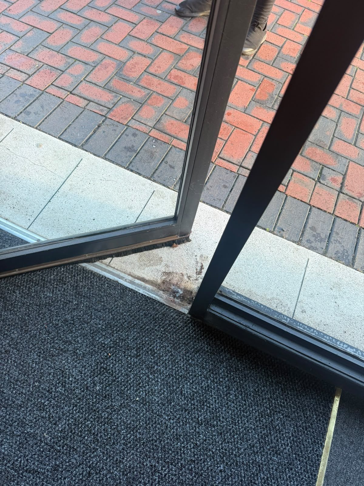 Corrosion at the foot of a commercial door frame at the threshold where the hinge fixing had failed