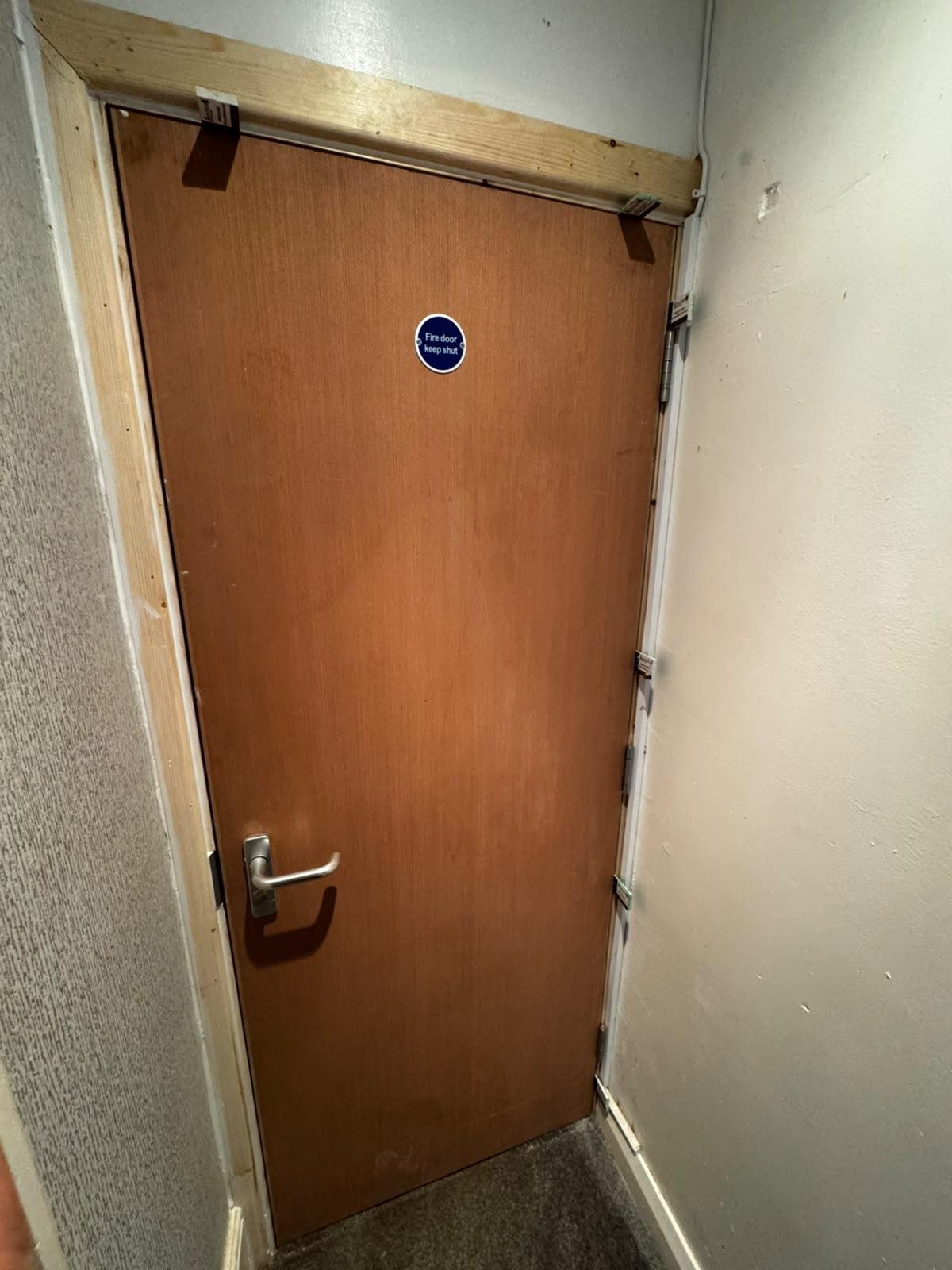 Plywood flush FD30 fire door with a lever handle and a fire door keep shut sign, framed by bare timber architraves