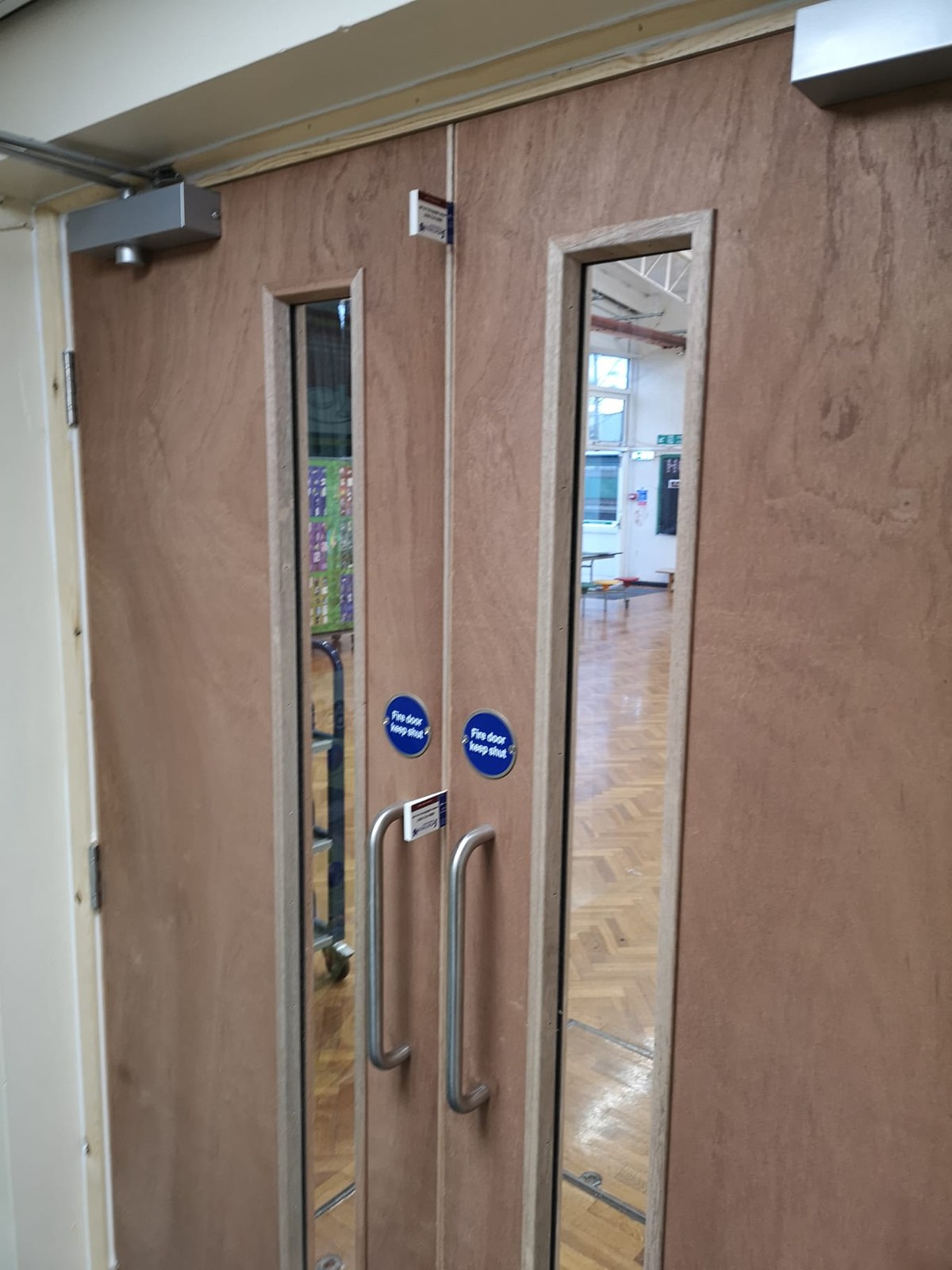 Plywood-faced fire doors with overhead closers at the head, pull handles and fire door keep shut signs, in a bare timber lining