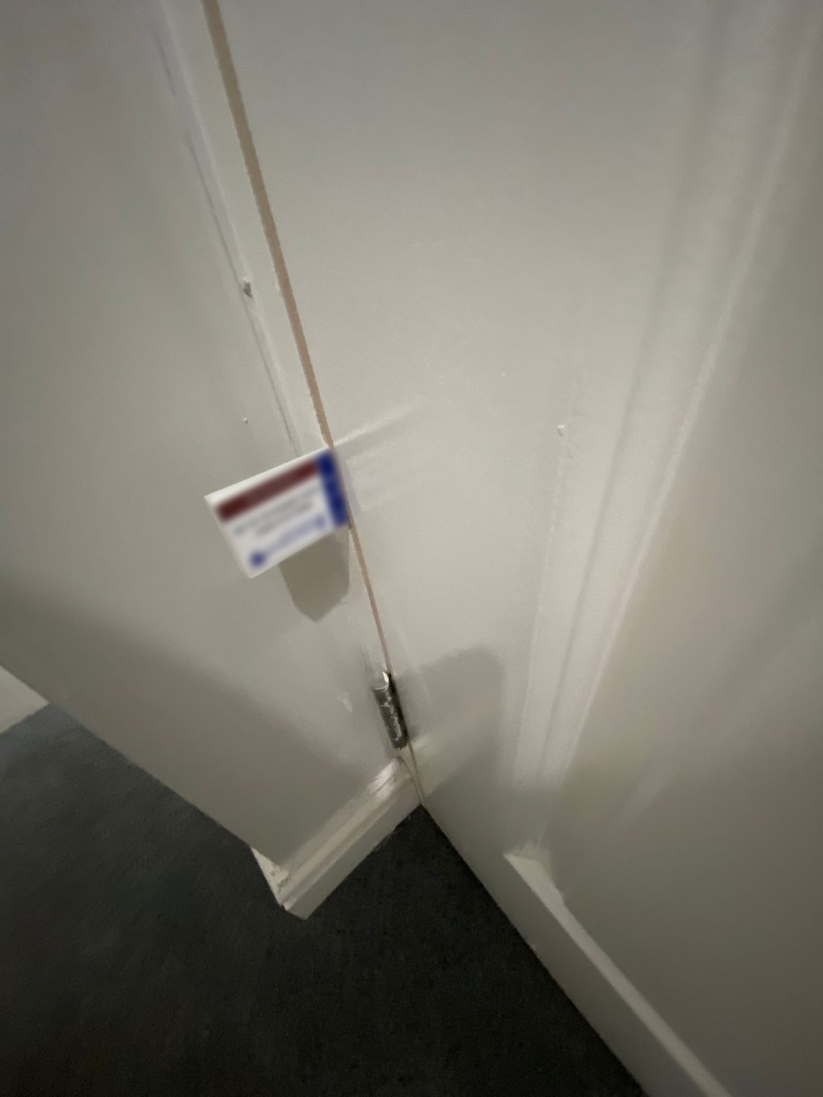 Gap gauge pushed into the gap down the hinge side of a white door, above the bottom hinge and the skirting