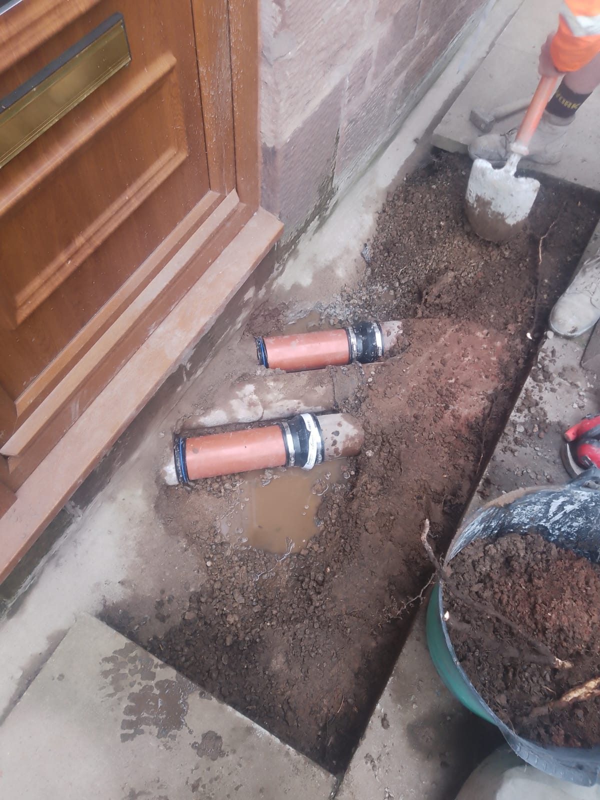 New drainage pipe sections laid in an open trench beside a doorstep, joined with black flexible rubber couplings