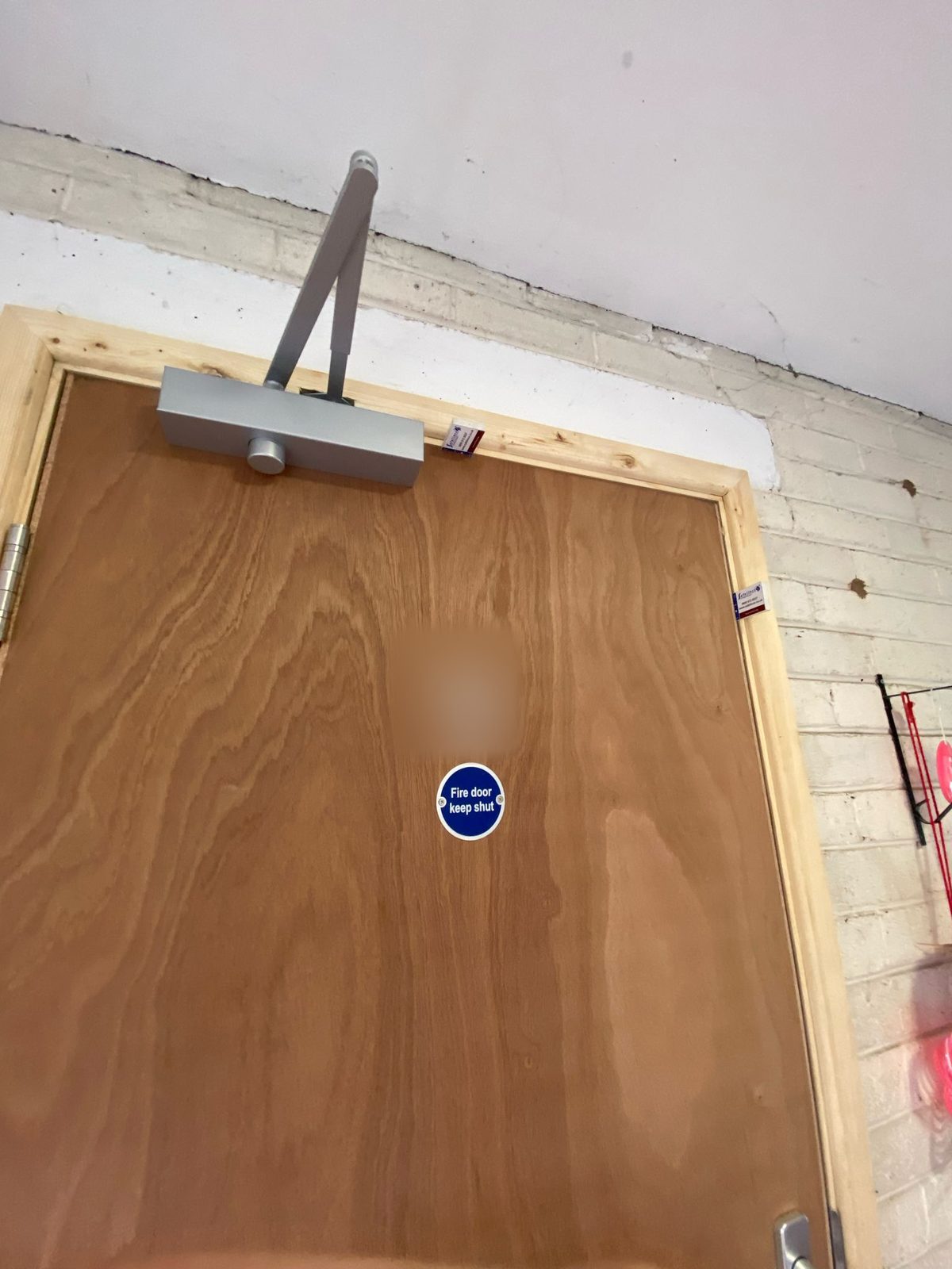 Overhead self-closing device at the head of a new plywood FD30 fire door, with a fire door keep shut sign on the leaf