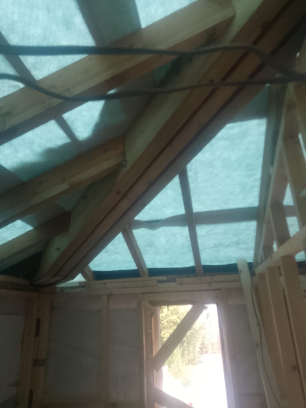 New timber hip and rafter structure inside a garage roof during rebuilding, with breathable roofing membrane above