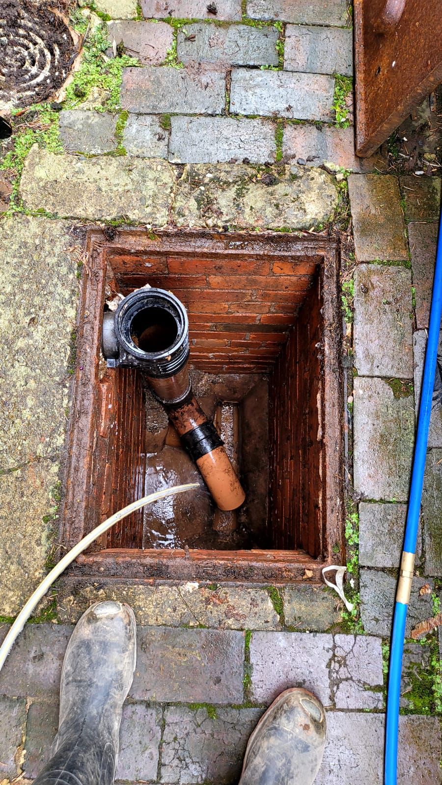 High-pressure jetting hose clearing a drain in a brick inspection chamber