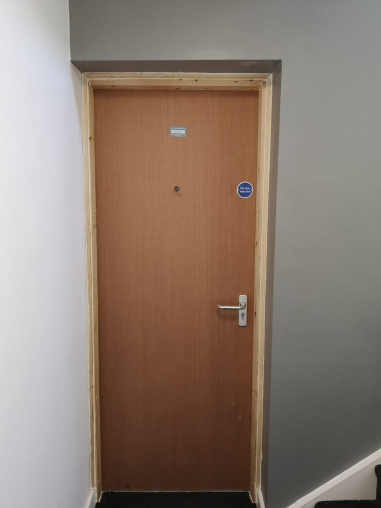 Veneer flat entrance fire door with spyhole, lever handle and fire door keep shut sign in a communal stairwell Veneer flat entrance fire door with spyhole, lever handle and fire door keep shut sign in a communal stairwell