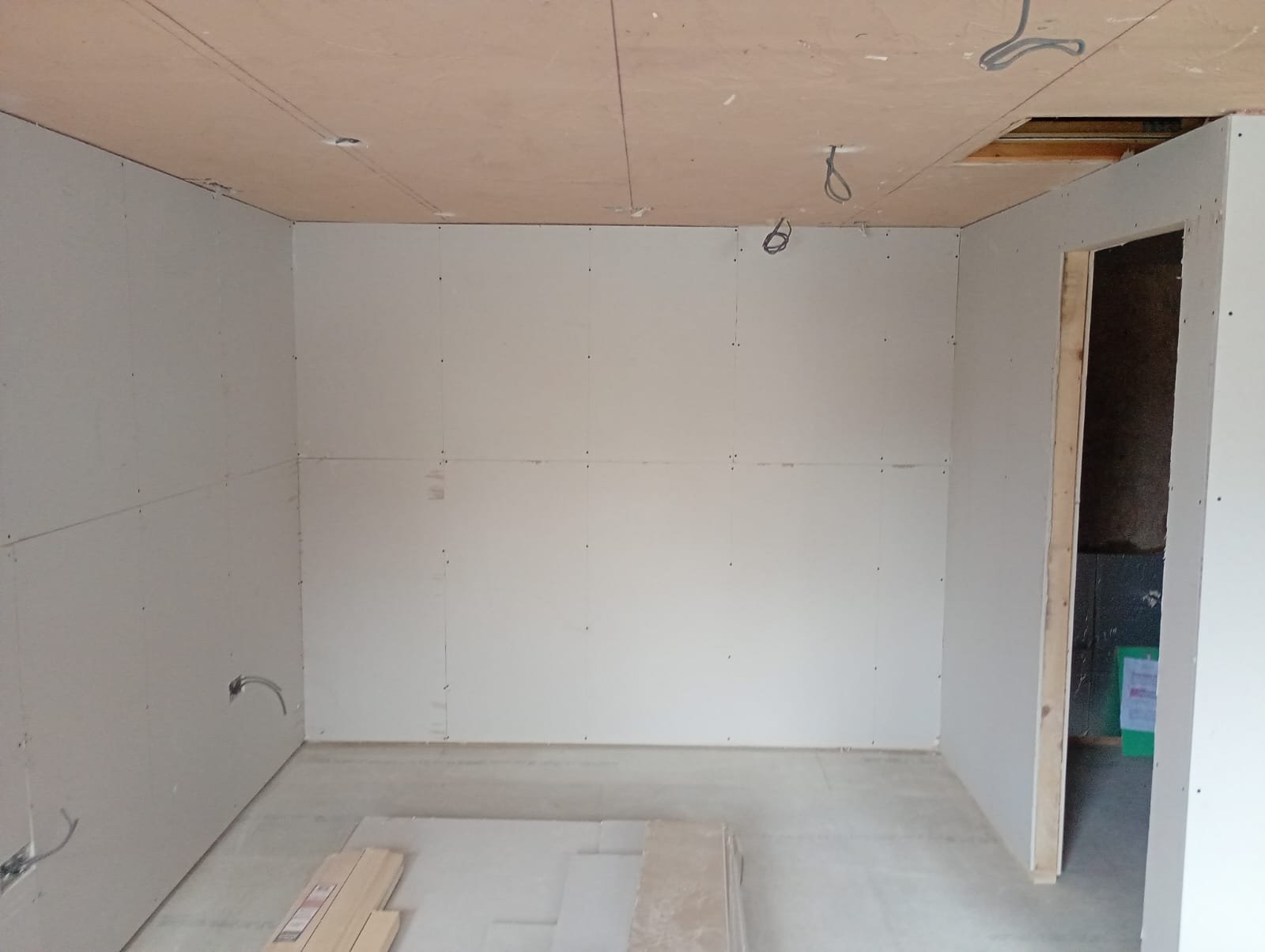 Converted garage interior lined throughout in plasterboard with a doorway through to a second room