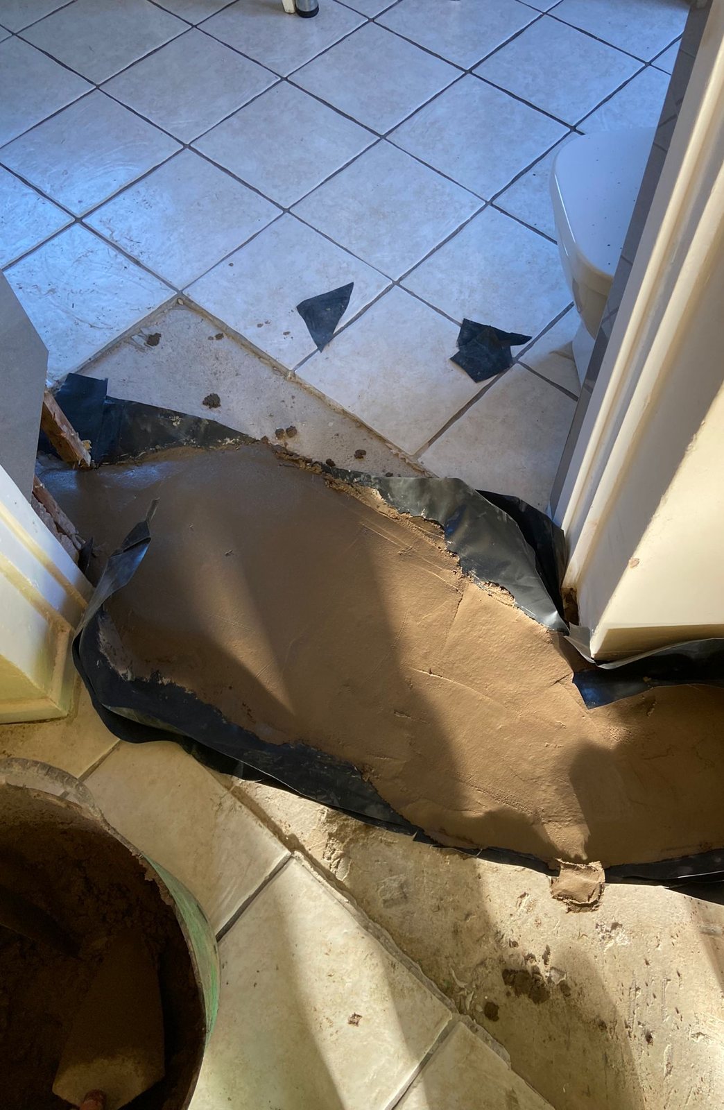 Fresh concrete laid in an opening in a tiled floor, with the edge of a black membrane showing around it