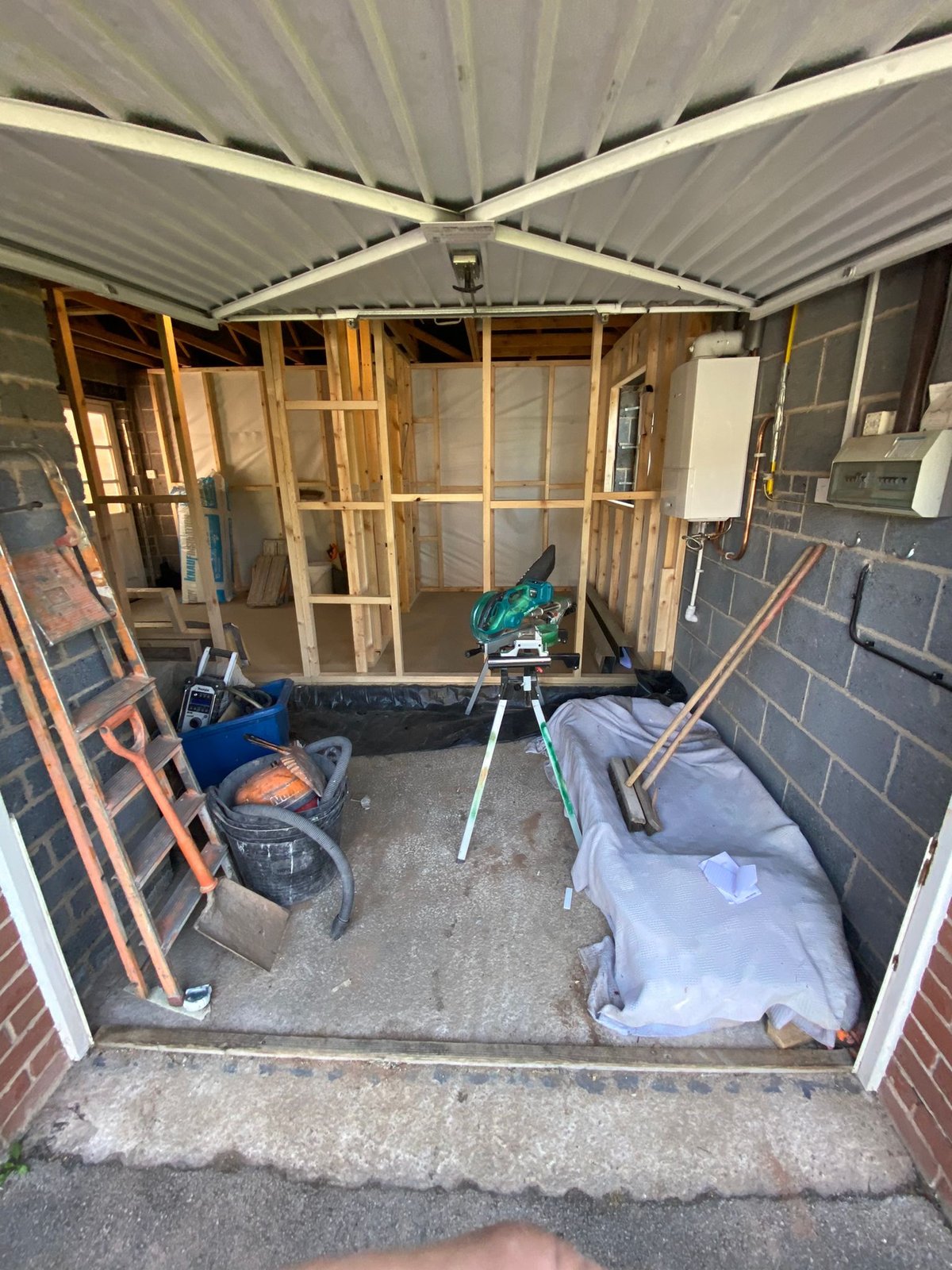 Timber stud walls built inside a garage during a partial conversion, with the up-and-over garage door still in place at the front