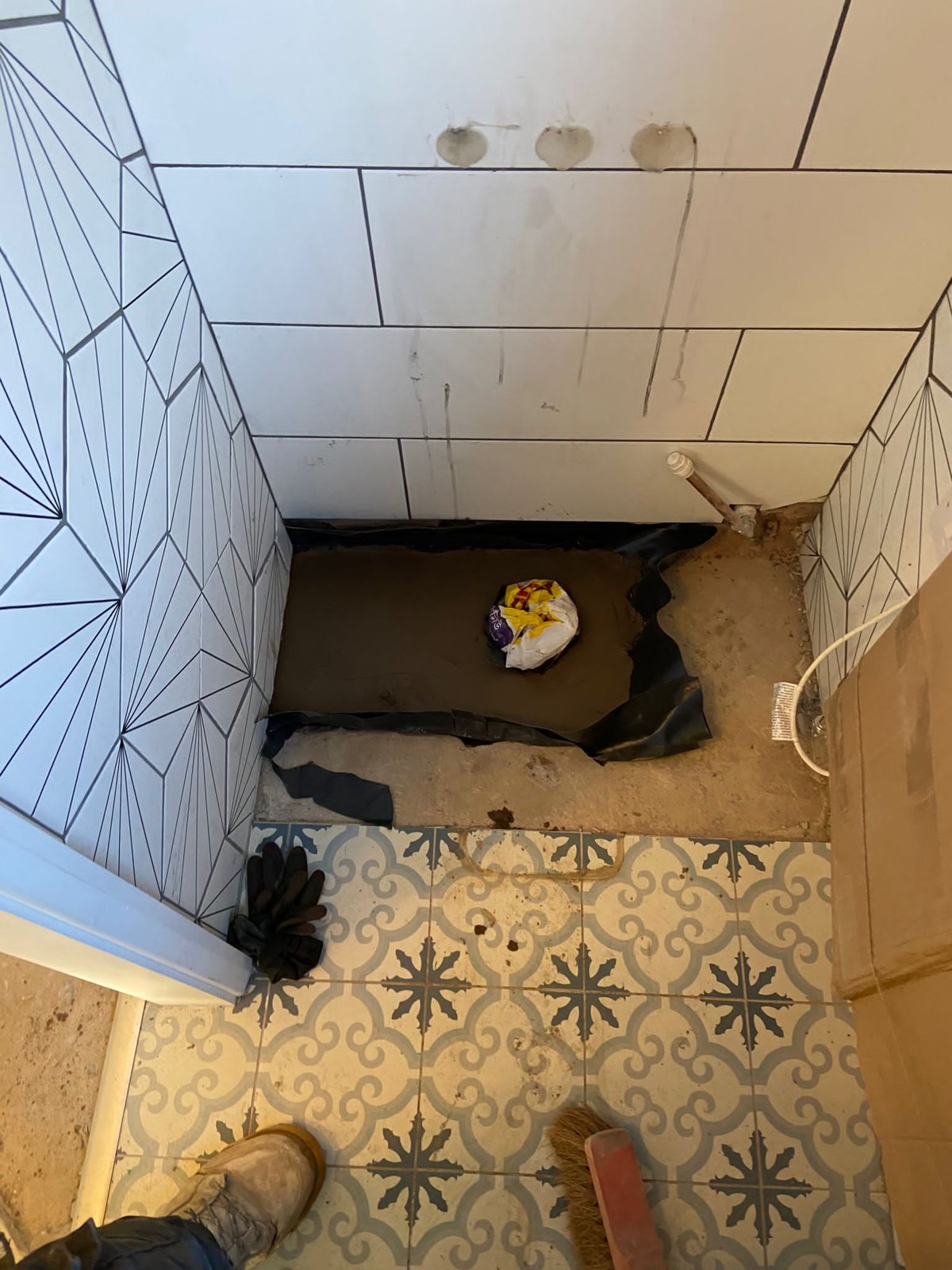 Tiled alcove with fresh concrete laid over a black membrane around a capped waste pipe in the floor