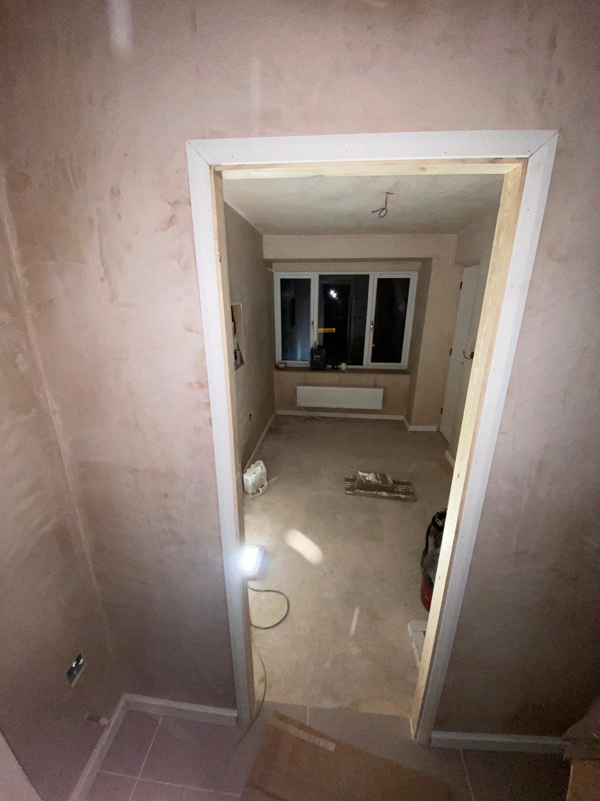 View through a newly formed doorway into a plastered ground-floor bedroom with a radiator beneath the window