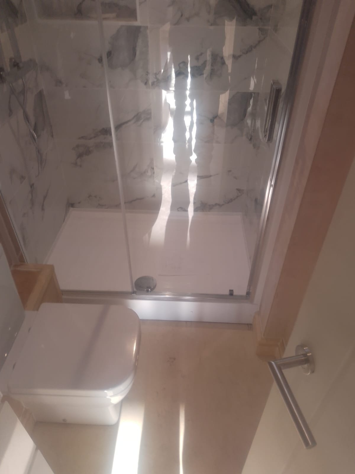 Finished shower room in a converted garage with a glazed shower enclosure, marble-effect tiling and a wall-hung WC