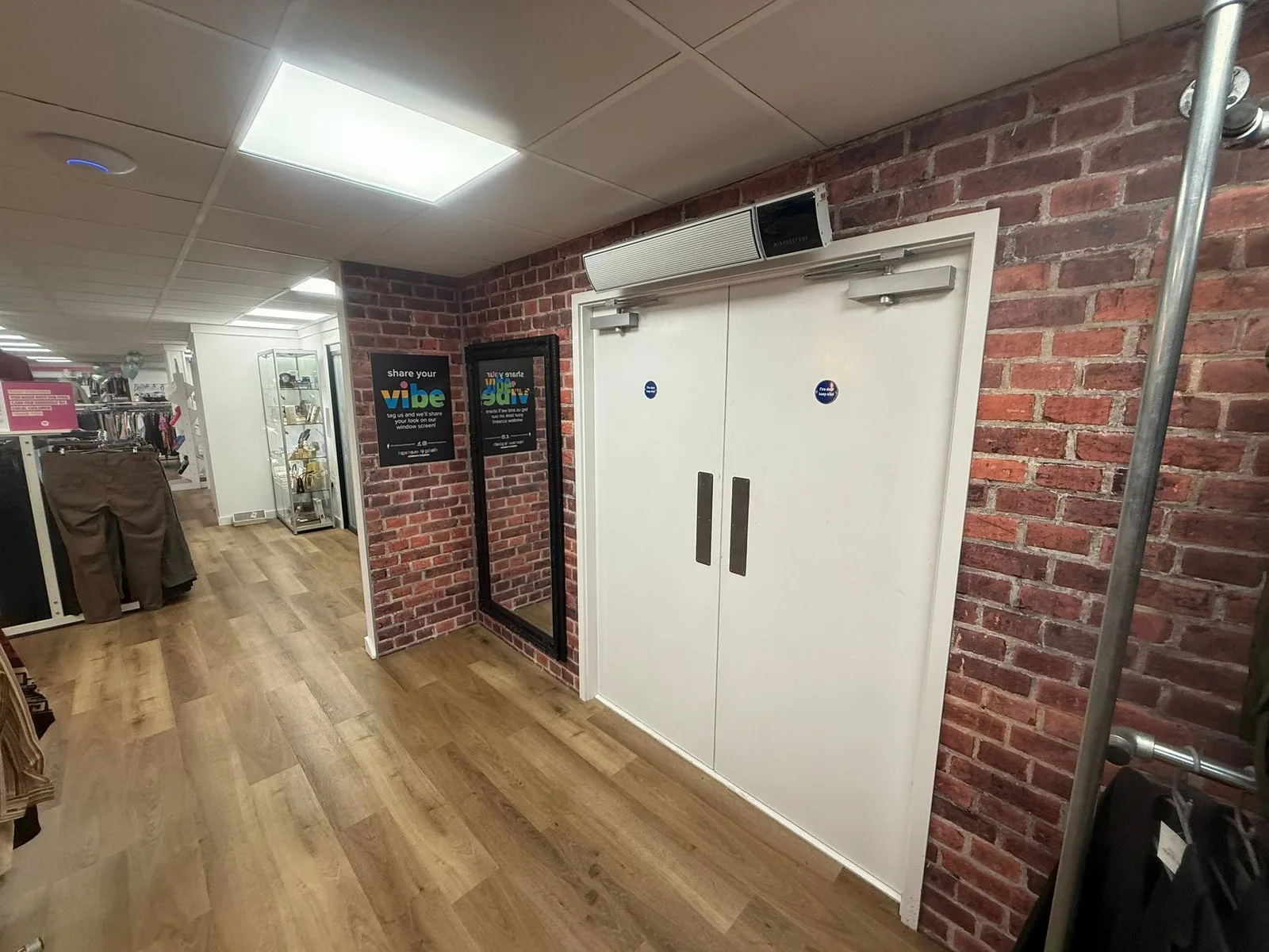 Pair of white fire doors with overhead closers fitted in a retail shop, brick-slip walls either side