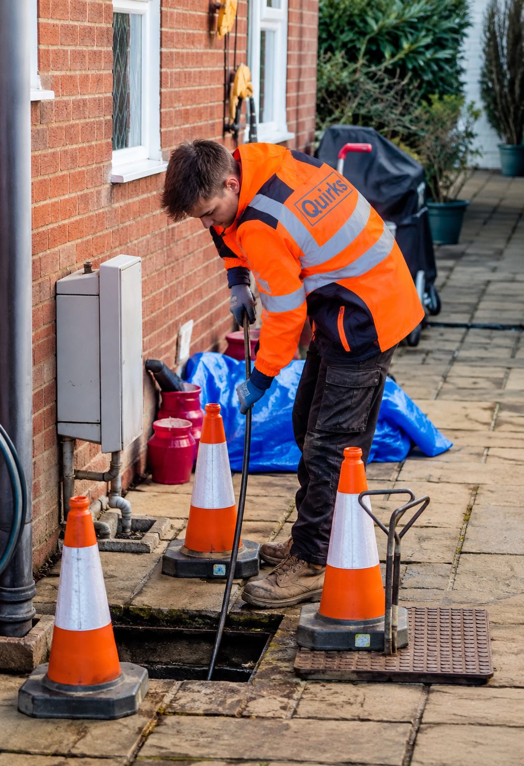 Quirks operative rodding a drain through an open inspection chamber, with the area coned off
