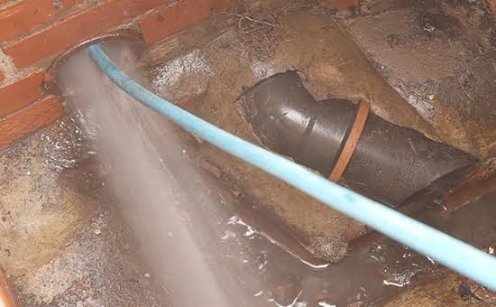 Jetting hose clearing a drain in a brick inspection chamber