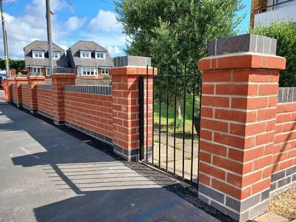 Red brick garden wall with a grey brick plinth and capped brick piers either side of a black metal gate