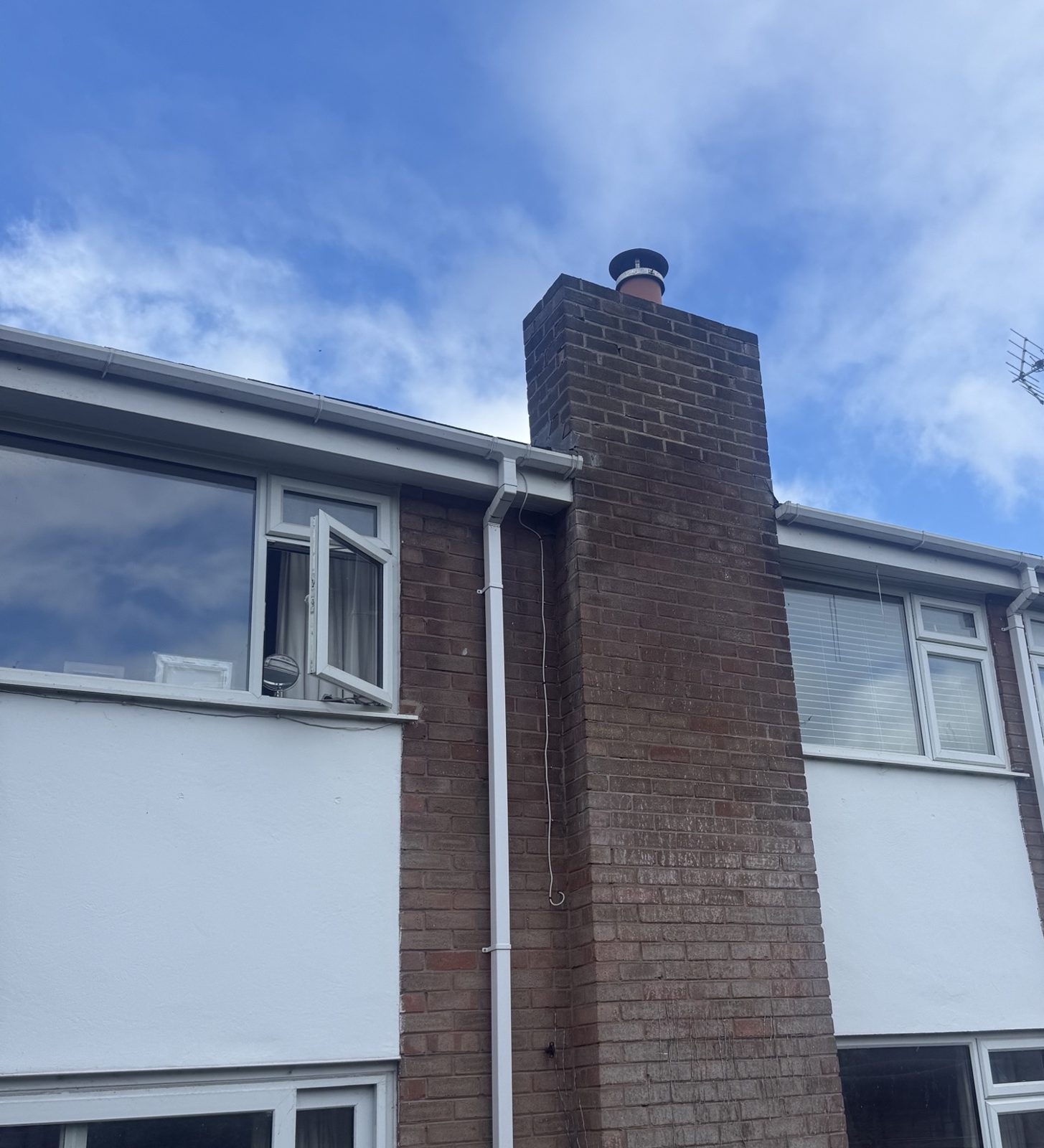 Rear of a row of brick terraced houses with white rendered panels below the upstairs windows and a tall brick chimney stack