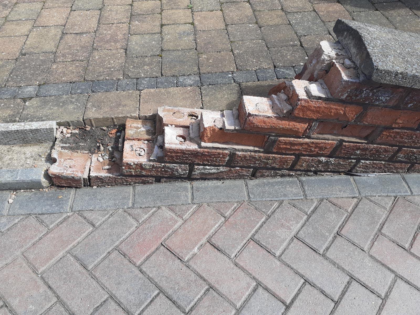 Low brick garden wall beside a block-paved drive with its end collapsed, bricks broken and the coping slab displaced