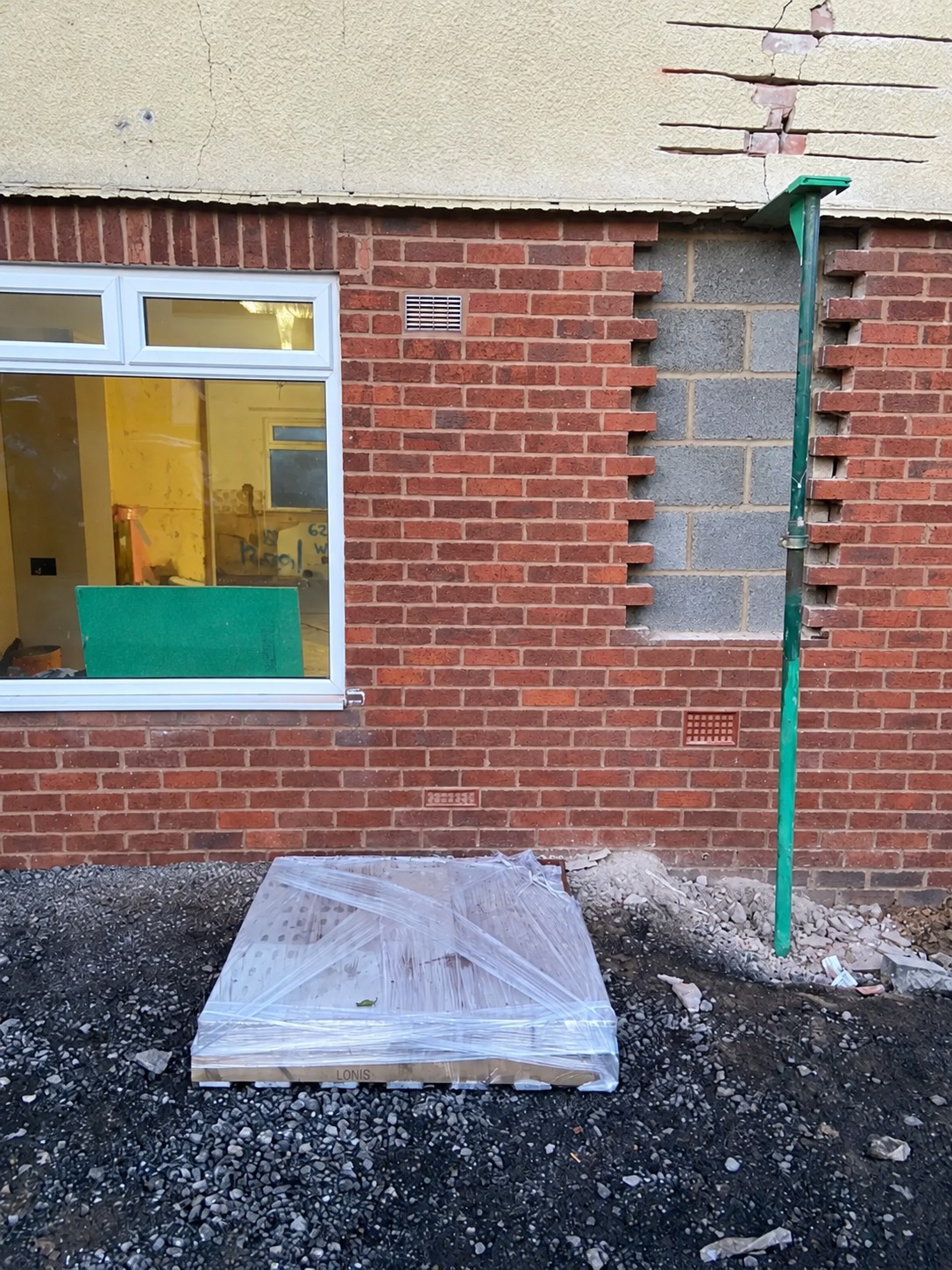 External brick wall during repair works, showing a neatly rebuilt section of grey concrete blockwork, stepped brickwork edges, a white uPVC window and green downpipe.