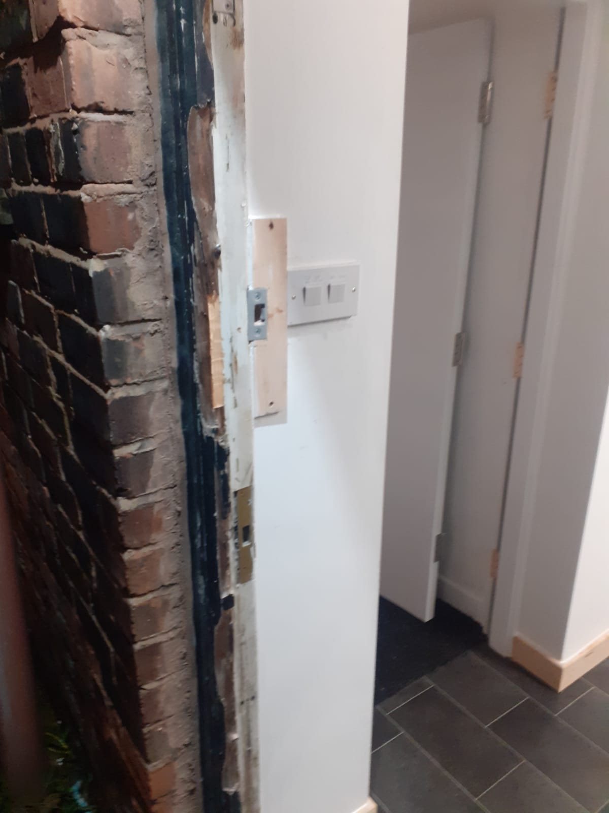 Door frame made good at the keep, with a new strike plate fitted on a timber packer beside old brickwork