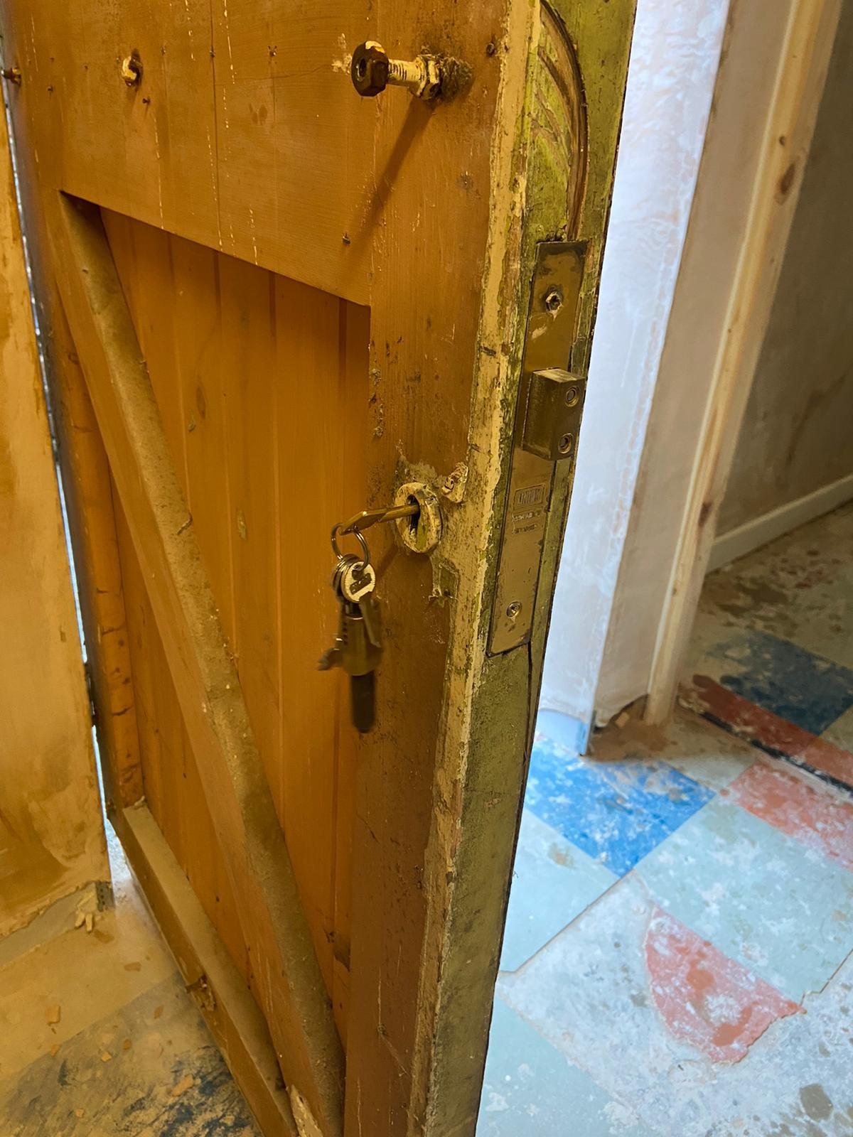 Old mortice lock exposed in the edge of a stripped timber door, with keys in the keyhole
