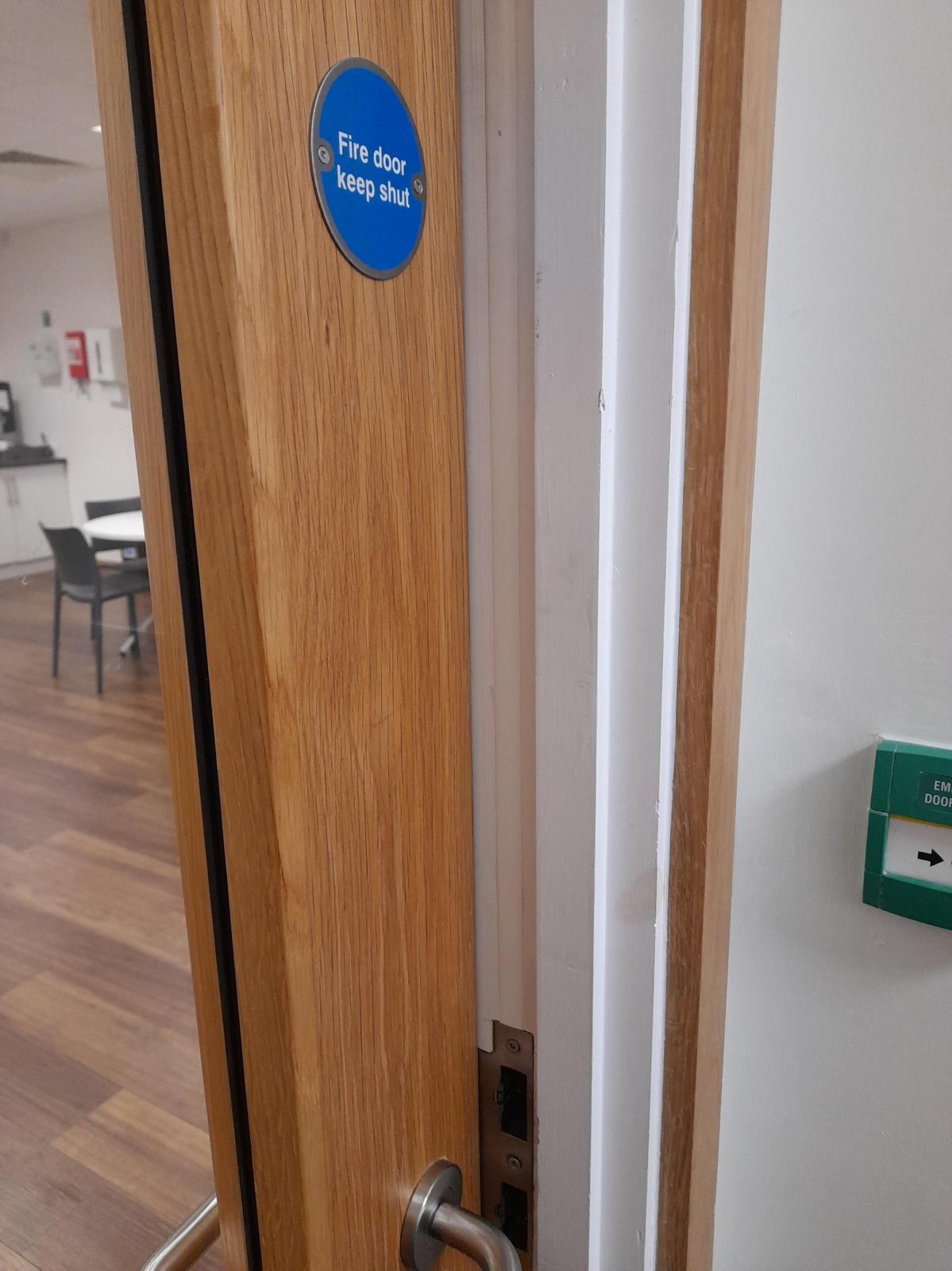 Edge of an oak fire door with a Fire door keep shut sign, lever handle and latch, open against its frame