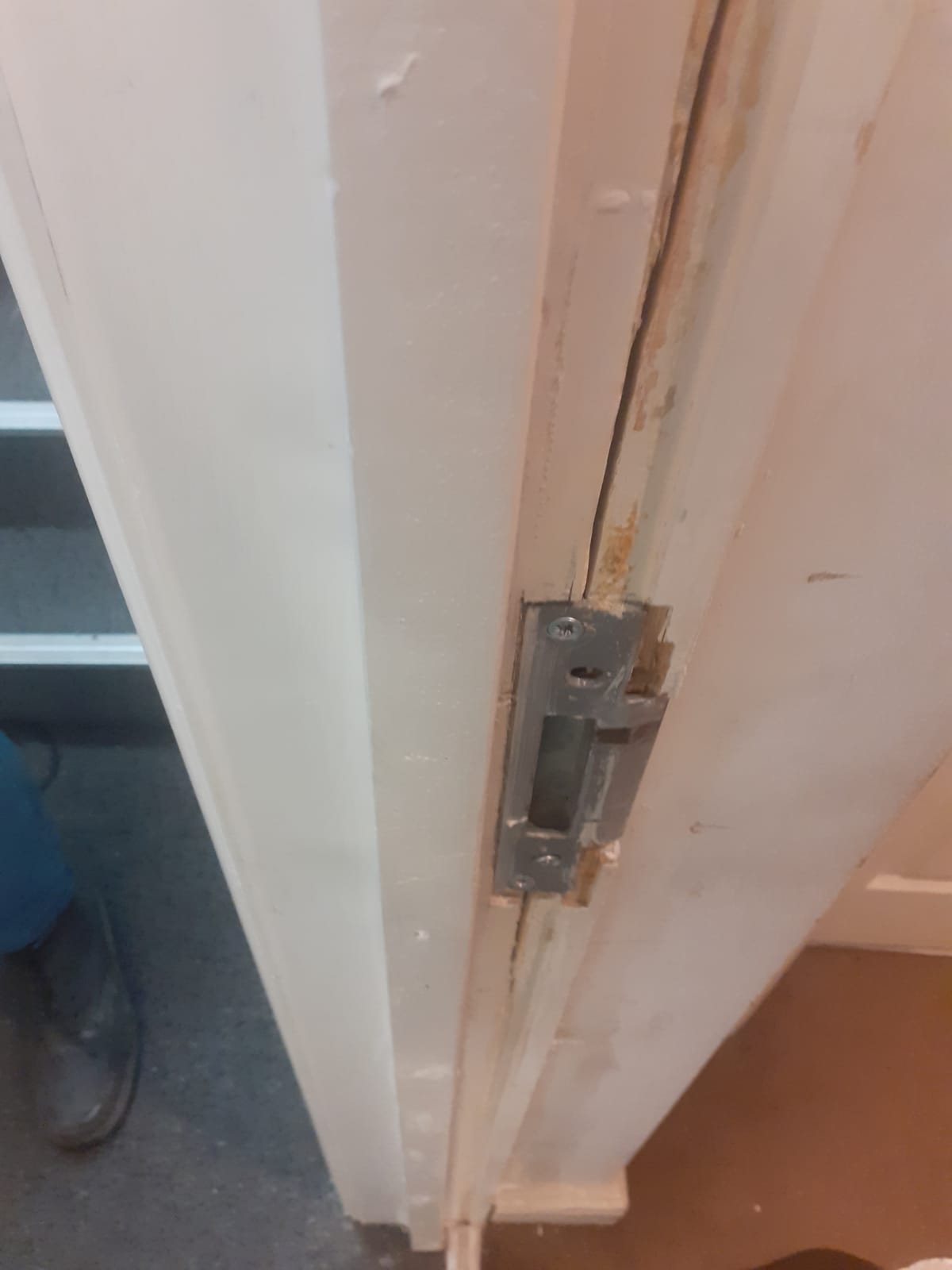 Door frame split at the keep, with the strike plate loose and the timber torn